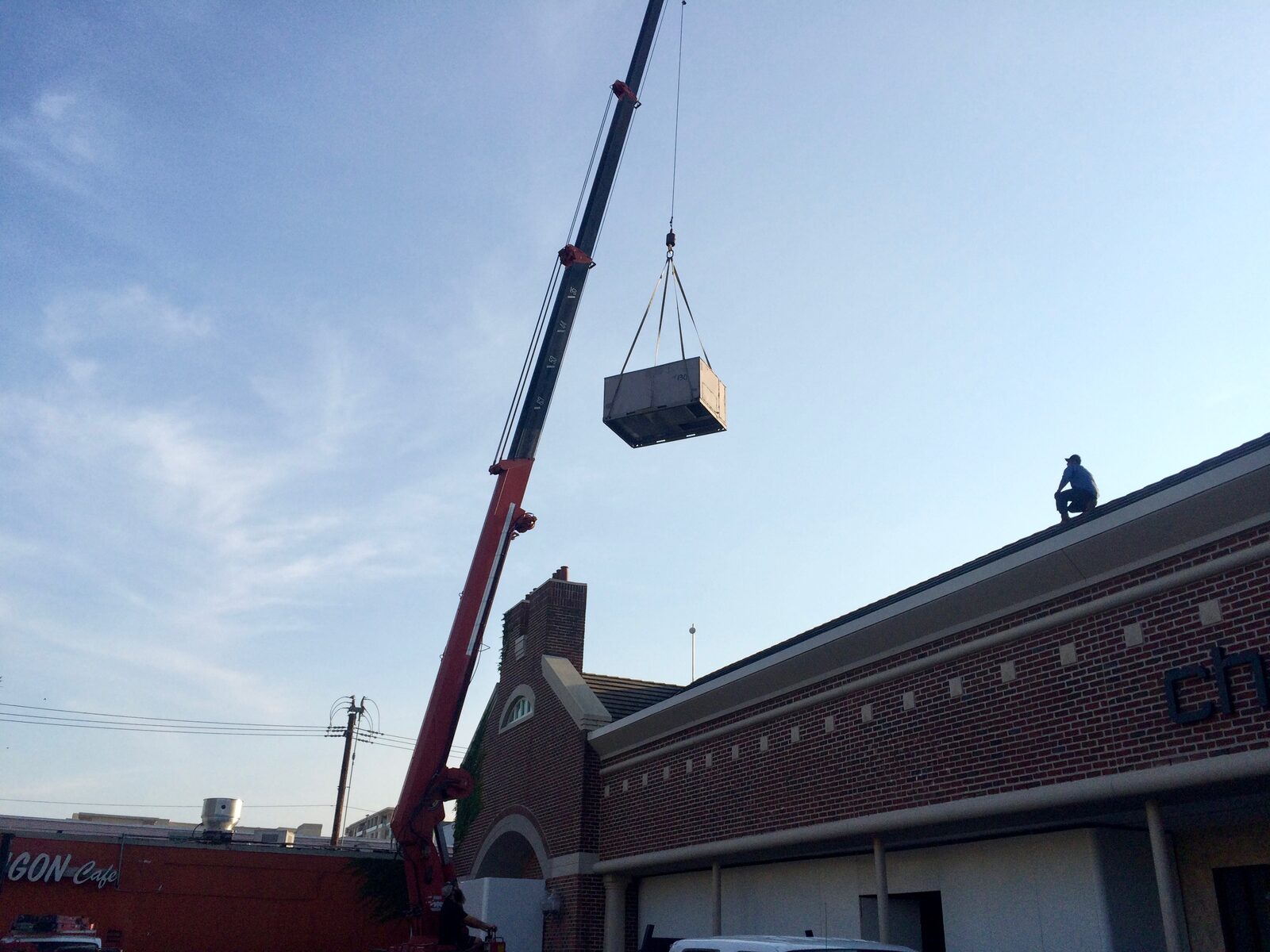A crane lifting a rooftop unit over a brick commercial building
