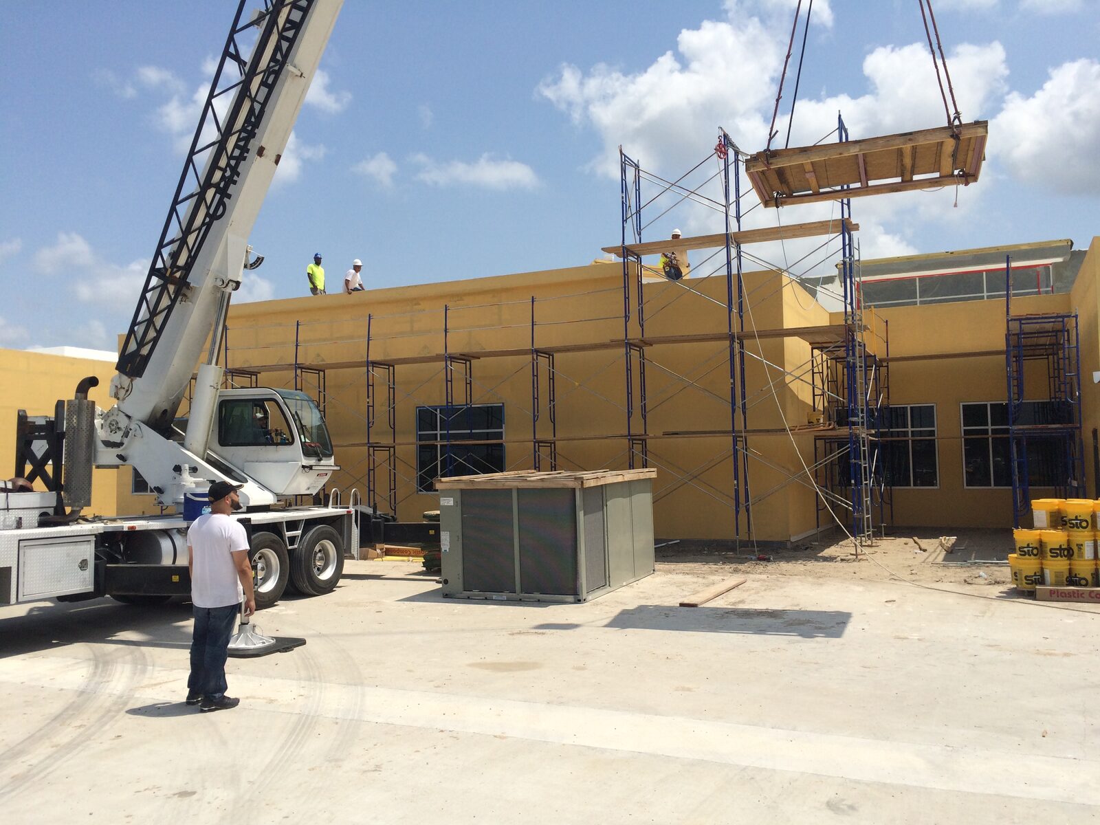 A crane lifting a rooftop unit onto a commercial building still under construction