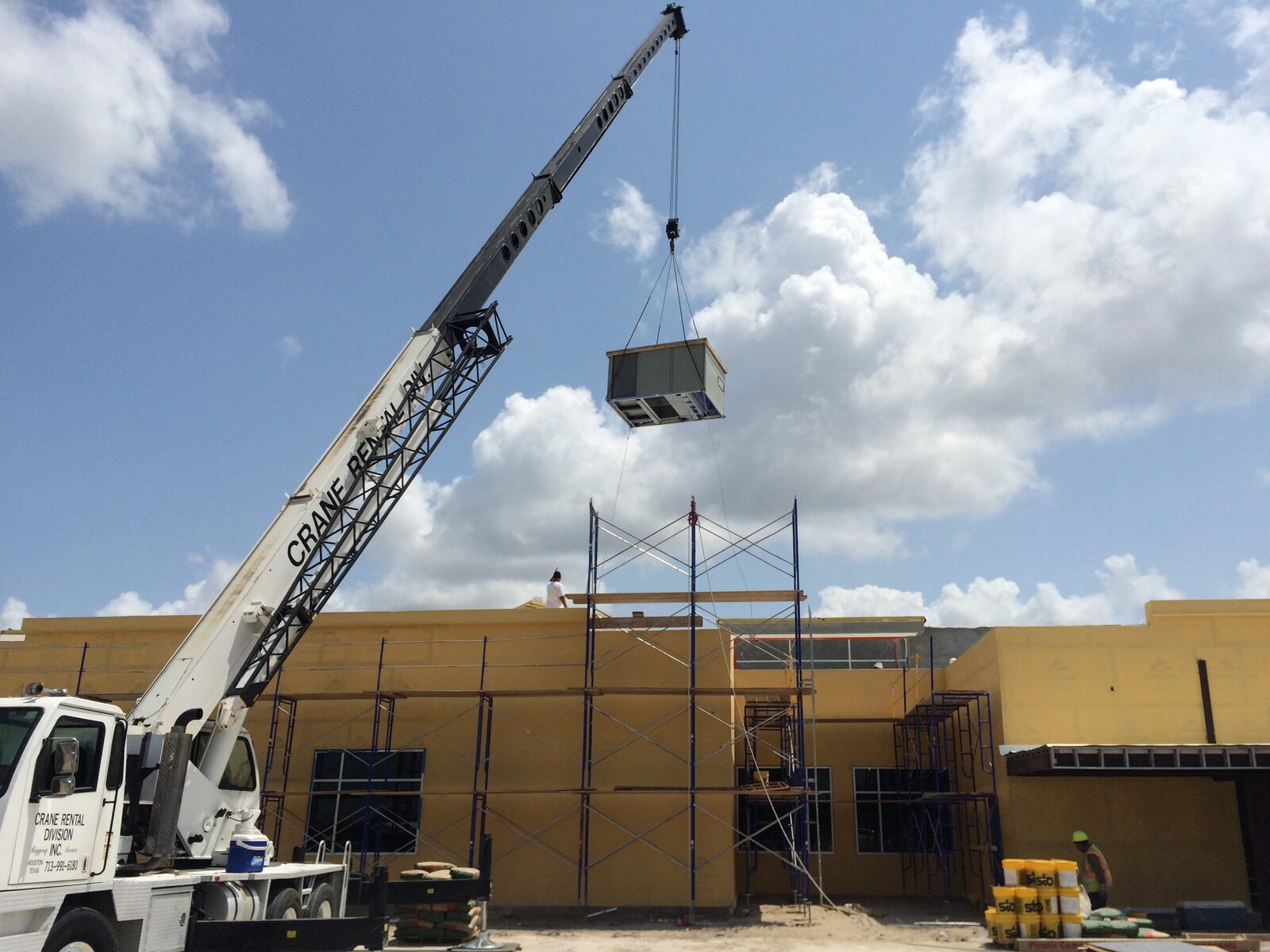 A crane lowering a rooftop unit onto a commercial building