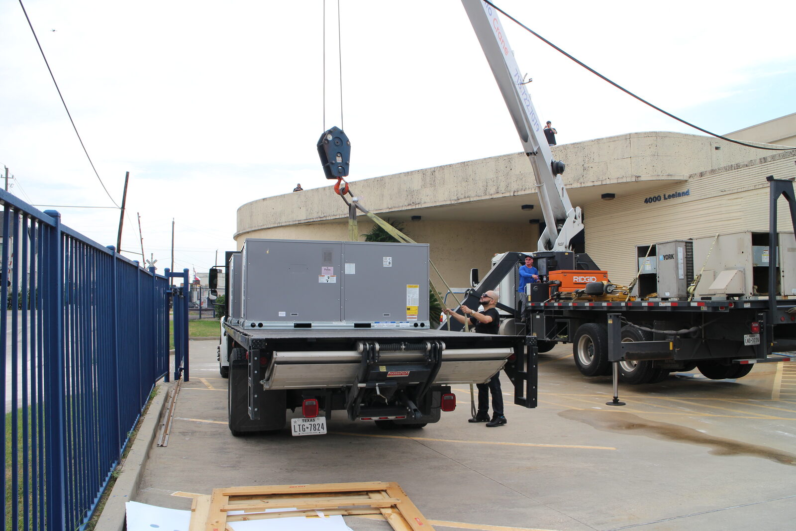 A crane truck parked at a commercial site with a rooftop unit on the bed