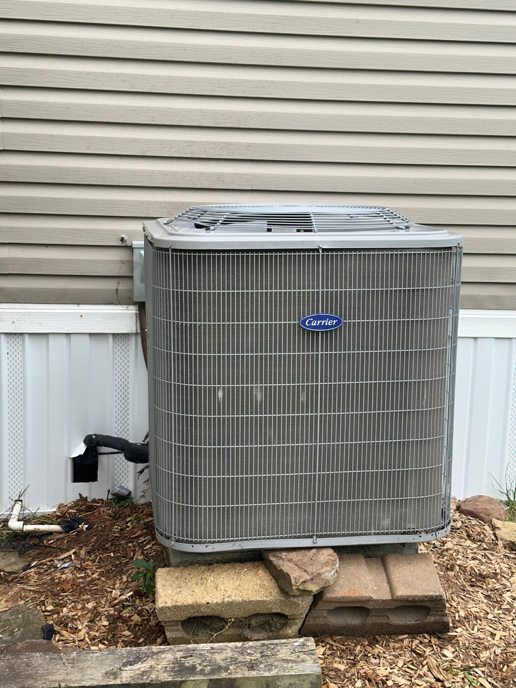 A residential condensing unit standing beside a wooden fence