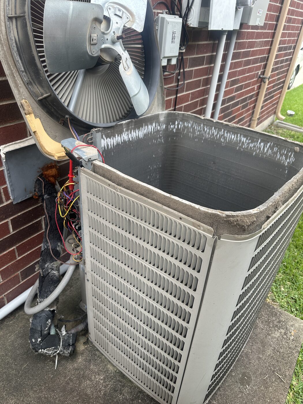 A residential condenser coil and disconnect on the side of a brick house