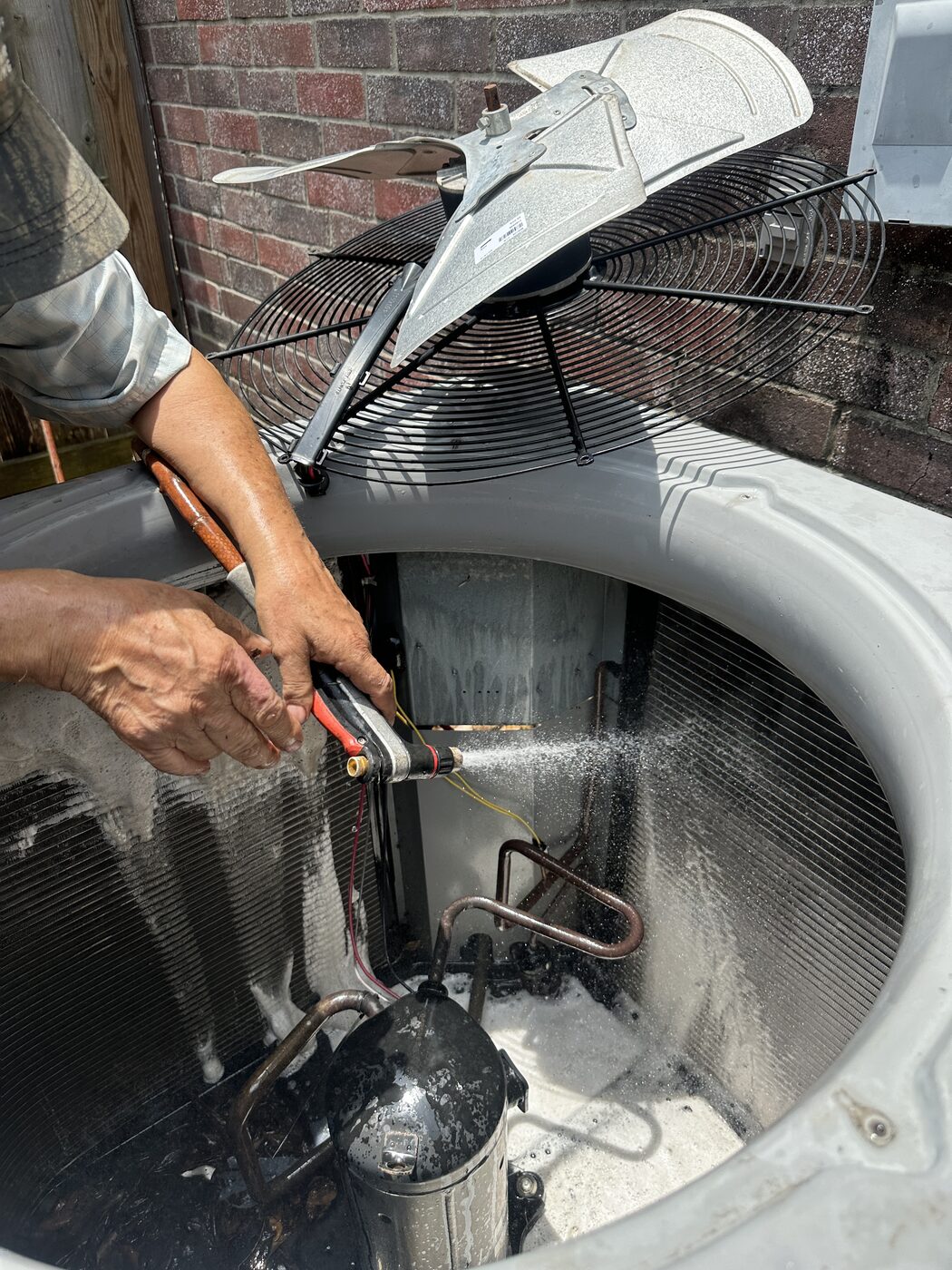 A hand washing down a residential condenser coil with water