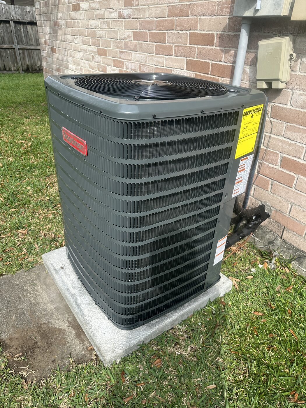 A residential air conditioning unit on a pad in a back yard