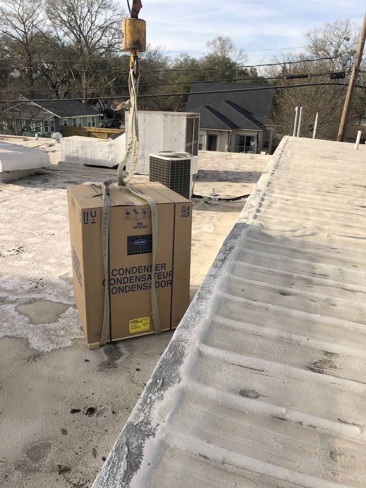 A boxed condenser being hoisted up to a commercial roof